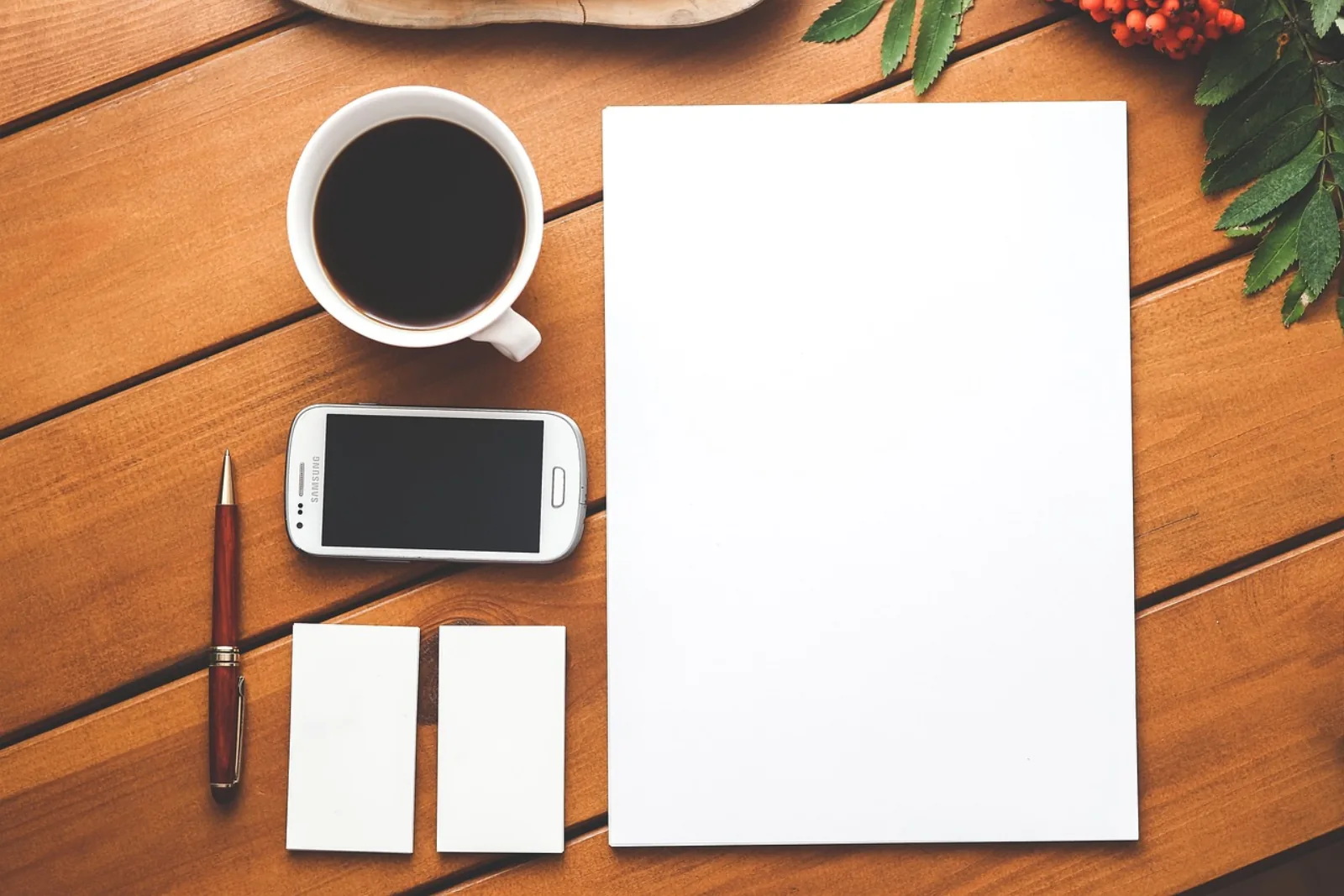 Kaffeetasse, Smartphone, Stift und leeres Blatt auf einem Holztisch – IT-Support-Kosten pro Stunde kalkulieren