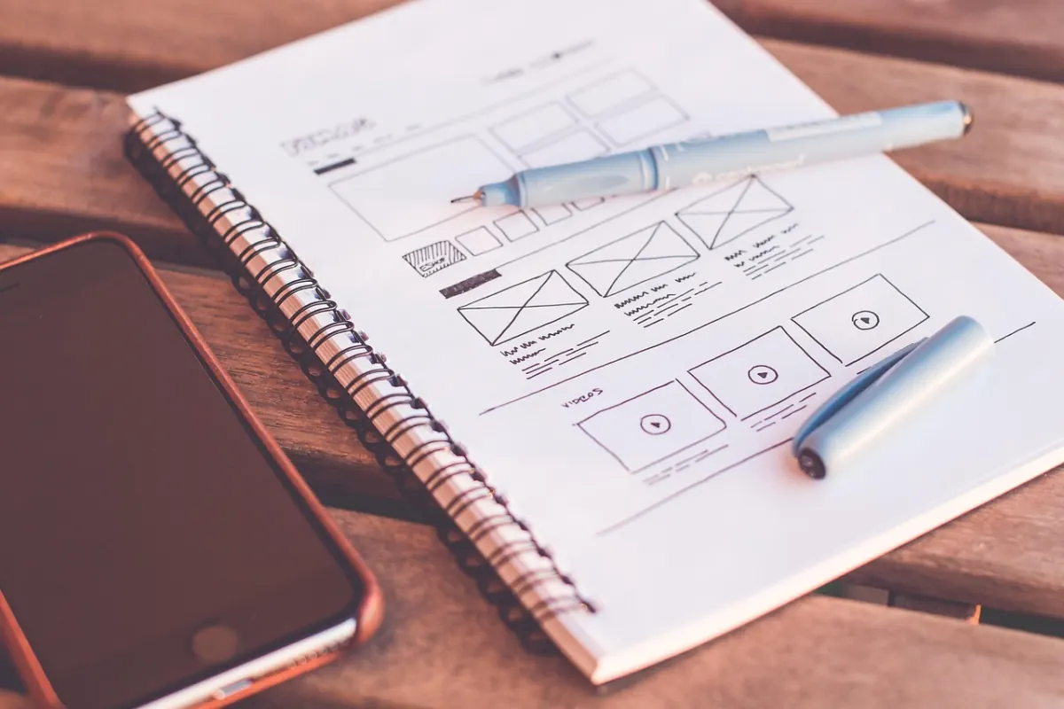 Notizbuch mit Skizze, Stift und Smartphone auf Holztisch – Kriterien für den Security-Awareness-Training-Vergleich